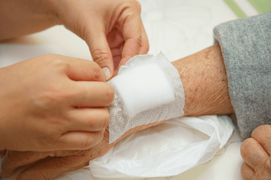 A wound dressing being applied to an elderly patient's arm.